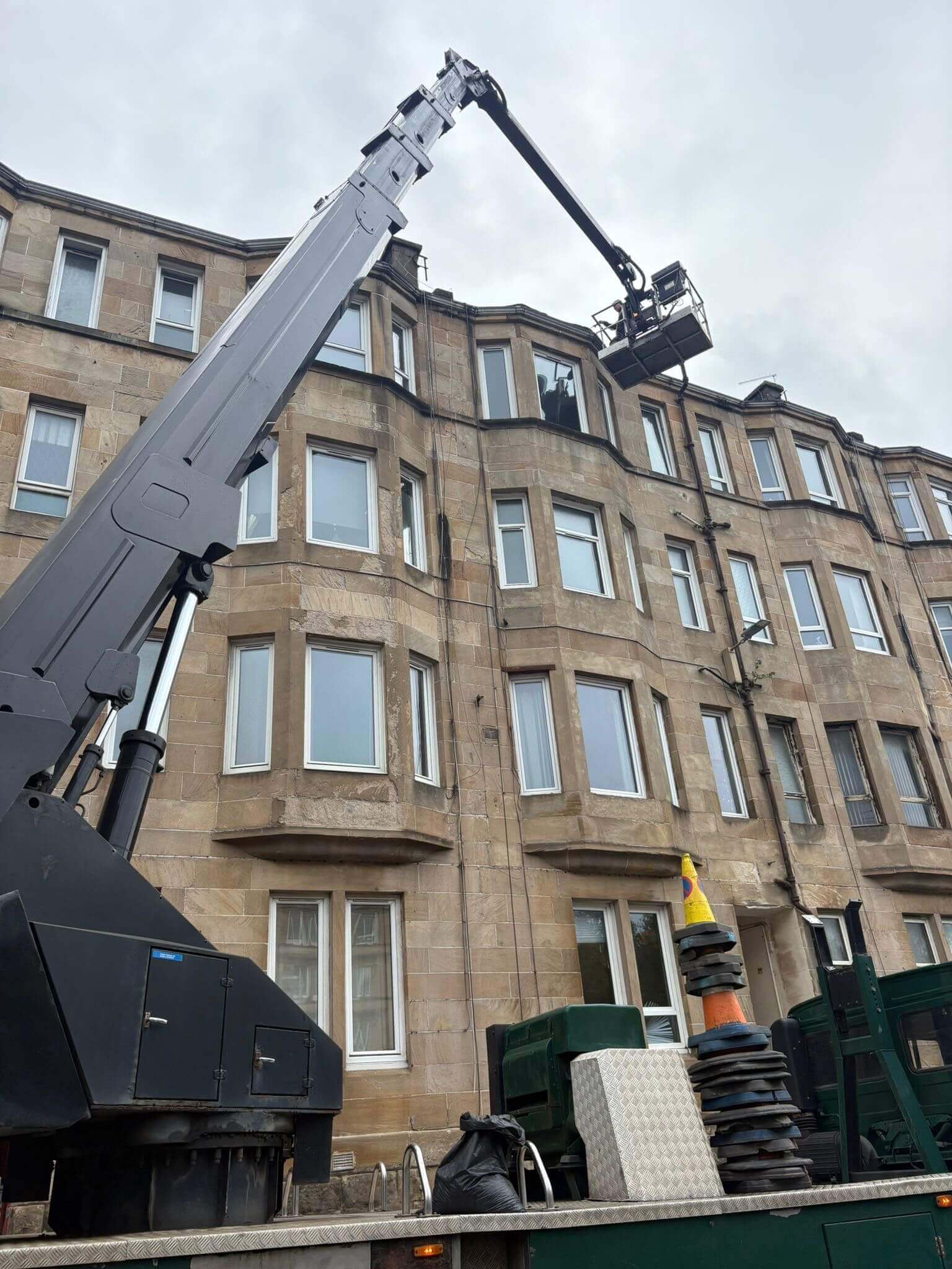 Operated truck-mounted cherry picker reaching 4-storey sandstone tenement building roofline in Glasgow
