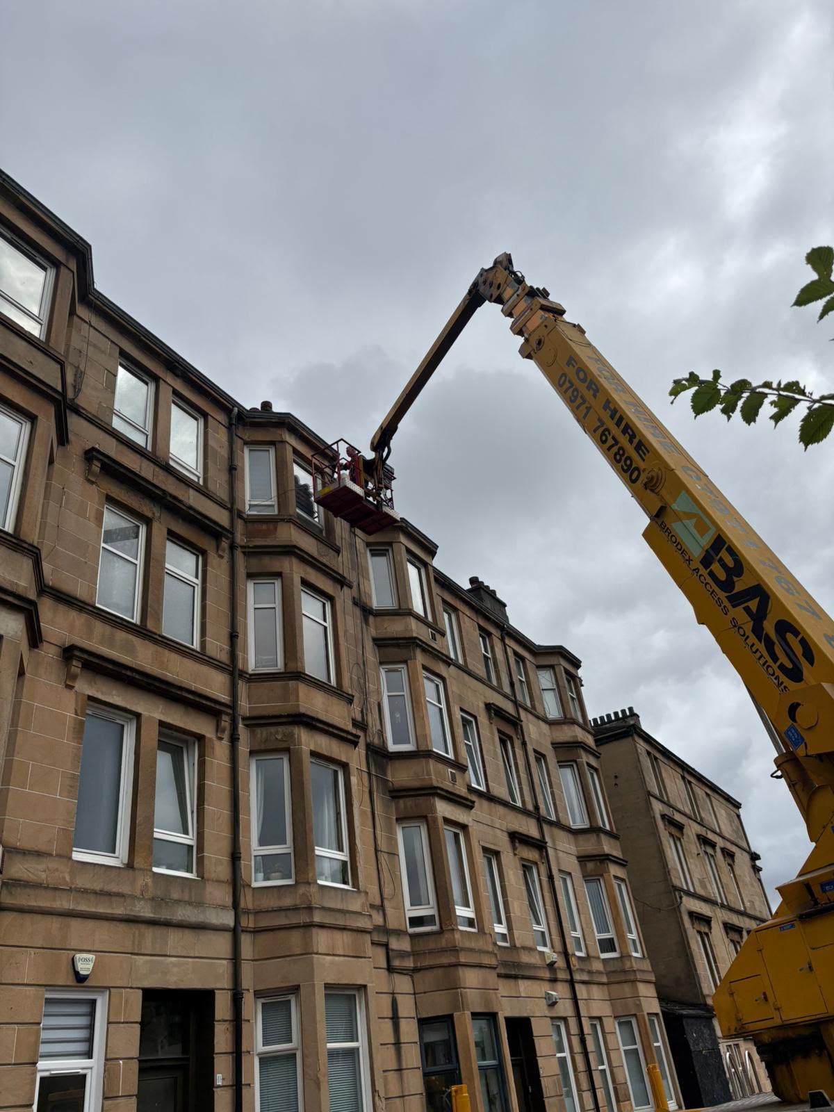 Operated truck mounted cherry picker platform extended to high level sandstone tenement roof in Glasgow